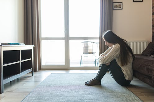 Sad and upset woman siting alone on the floor at home.