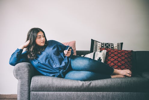 Beautiful plus size girl lying on the sofa with moblile phone. Toned picture