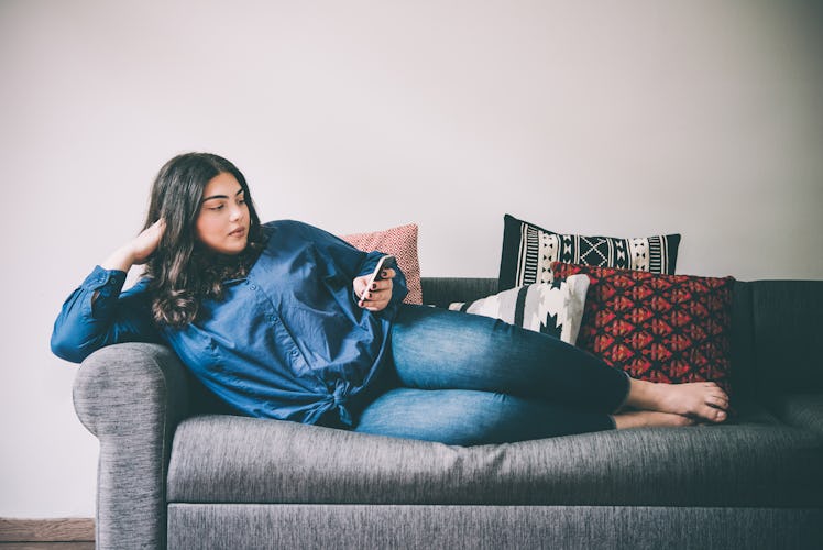 Beautiful plus size girl lying on the sofa with moblile phone. Toned picture