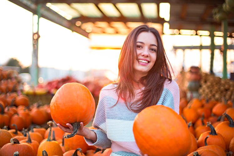 Young woman holding two pumpkins at a pumpkin patch, in need of Instagram captions for pumpkin patch...