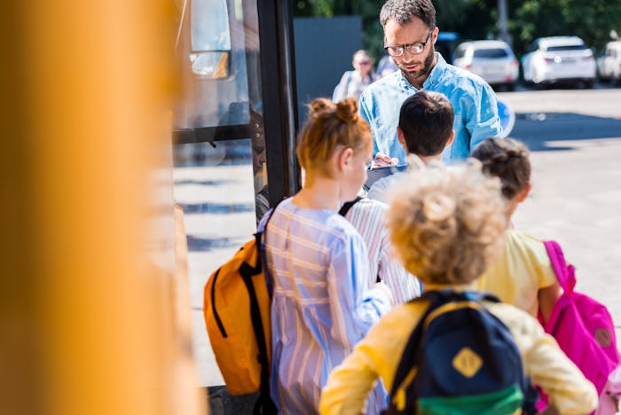 rear view of pupils entering school bus while teacher writing in clipboard