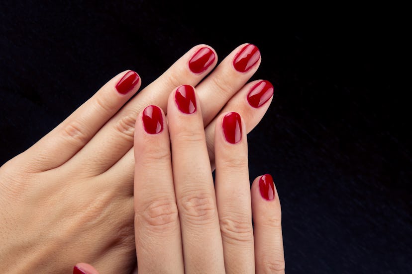 Pretty red painted short nails and hands isolated on black background