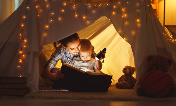 reading and family games in children's tent. mother and child daughter with  book and flashlight bef...