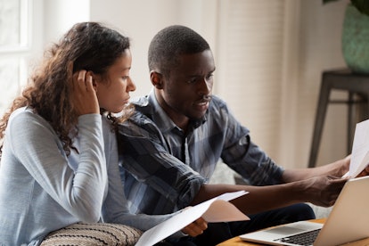 African Millennial stressed married couple sitting on sofa at home checking unpaid bills, taxes, due...