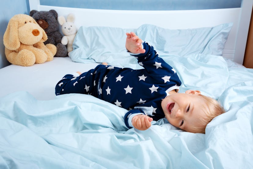 One year old baby in pyjamas lying in the bed with blue bedding