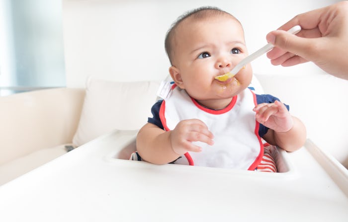 Mother feeding baby puree food on high chair