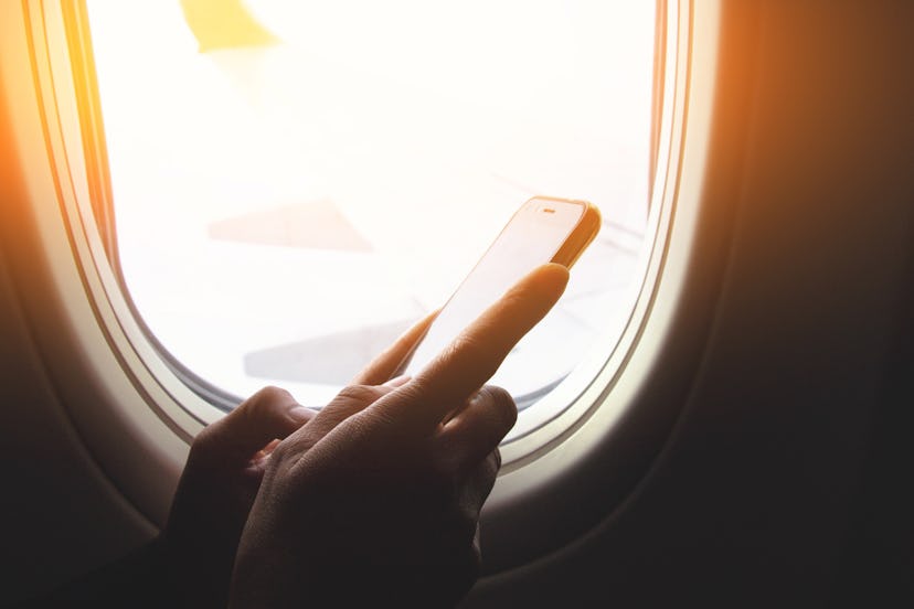 Hand using smart phones on board of an airplane near window seat and wing.
