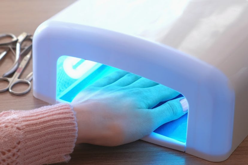 Woman includes lamp and dries her nails with shellac in UV lamp. Close-up.