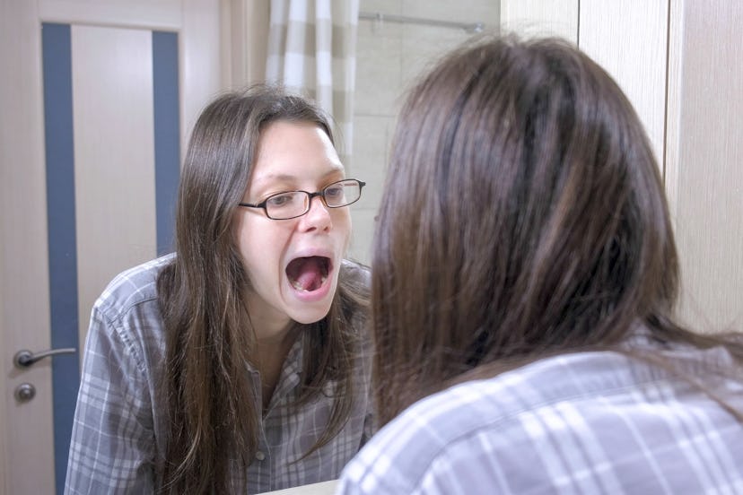 Woman looking on her teeth in the bathroom near the mirror and yawn.