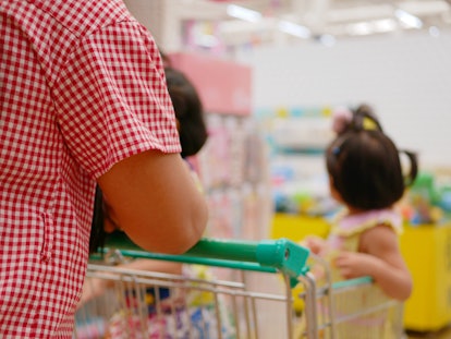 Selective focus of a mother doing shopping, pushing a shopping cart, with her two little daughters i...