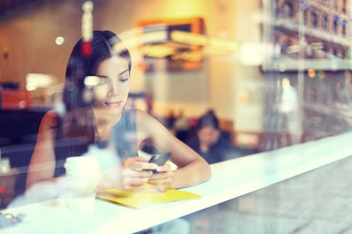 Cafe city lifestyle woman on phone drinking coffee texting text message on smartphone app sitting in...
