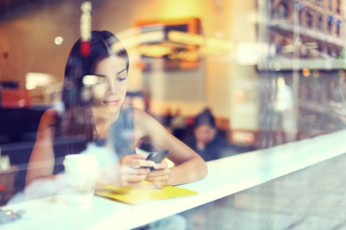 Cafe city lifestyle woman on phone drinking coffee texting text message on smartphone app sitting in...