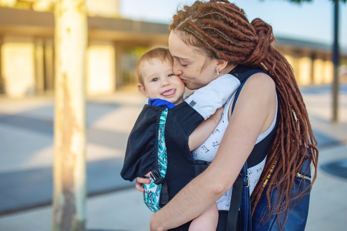 Young happy mom with baby son in ergo backpack travel together. The dark wall on the background. The...