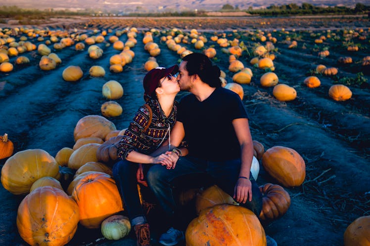 Couple in love kissing in a pumpkin patch farm, sitting in a pile of pumpkins for which they'll need...