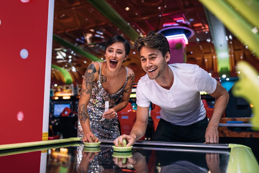 Couple playing air hockey game holding strikers at a gaming parlour. Excited man and woman having fu...