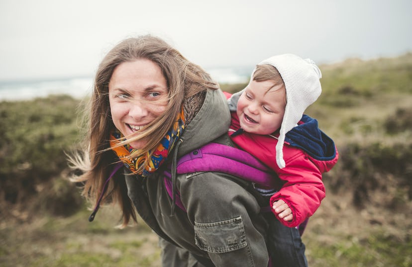 Mother carrying toddler on her back outdorrs, both are laughing, earthy boy names