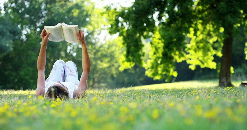 Young woman lying and reading her favorite book on a o green meadow covered with yellow flowers in a...