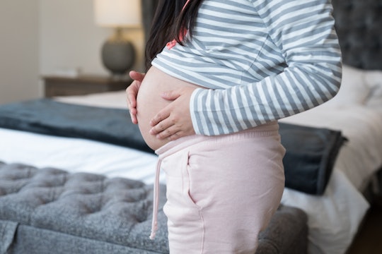 Mid section of pregnant woman touching her stomach in bedroom