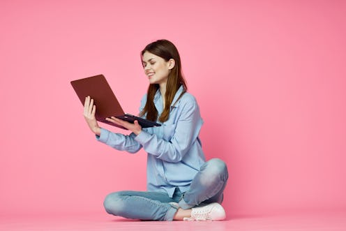 woman works with a laptop on a pink background