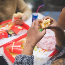 young african woman eating sandwich with friends in fast food – hungry, sharing, joyful