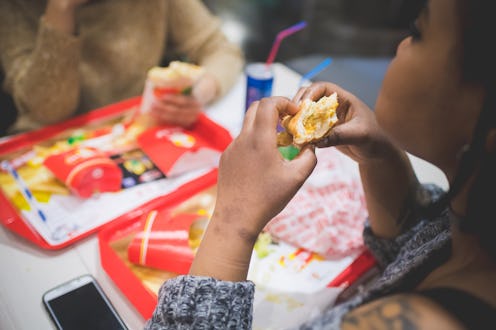 young african woman eating sandwich with friends in fast food – hungry, sharing, joyful