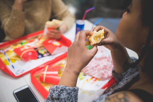 young african woman eating sandwich with friends in fast food – hungry, sharing, joyful