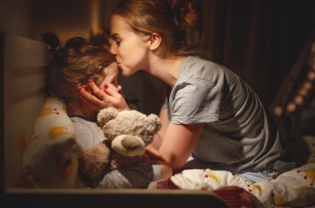 A mom kisses her child on the forehead in bed in a dark room, an example of getting reassurance that...