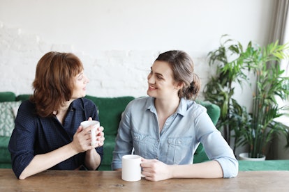 Beautiful mature mother and her adult daughter are drinking coffee, talking and smiling