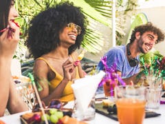 Group of multiracial friends gathered around a table in a garden on a summer day to share meal and l...