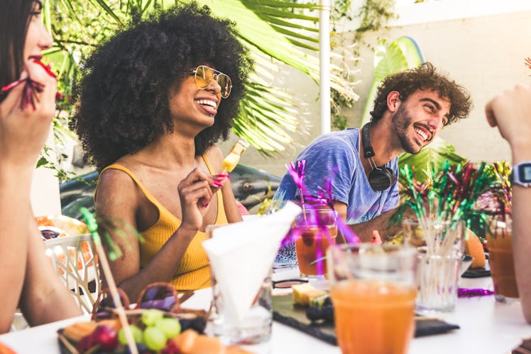 Group of multiracial friends gathered around a table in a garden on a summer day to share meal and l...