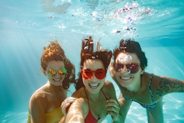 Cheerful women friends swimming underwater in pool taking selfie. Underwater selfie of happy females...