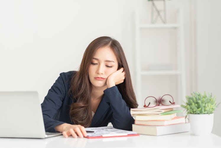 Bored young Asian business woman working with a laptop in the white room. Overworked, tired, Lazy em...