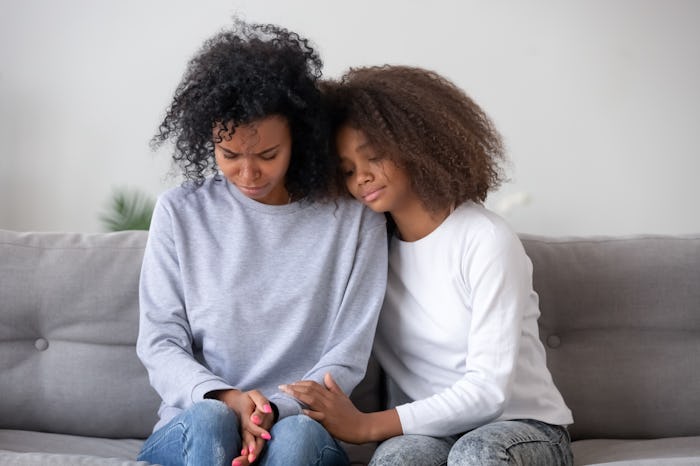 Sad african daughter and mother sitting on sofa, kid asks mother for forgiveness feel guilty apologi...