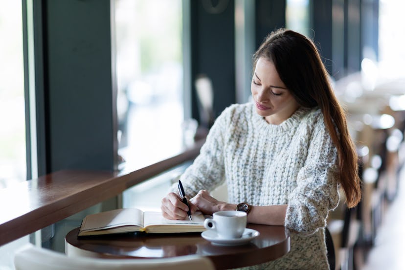 Young attractive woman writing diary in cafe