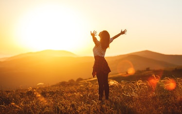 Happy woman jumping and enjoying life in field at sunset in mountains
