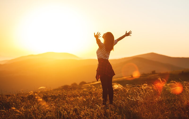 Happy woman jumping and enjoying life in field at sunset in mountains