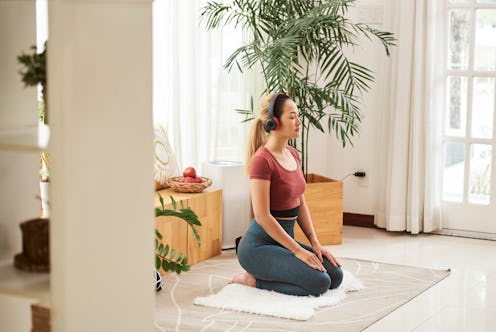 Young Asian woman in headphones sitting on fluffy rug and meditating