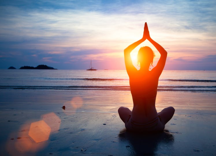 Silhouette young woman practicing yoga on the beach at sunset.