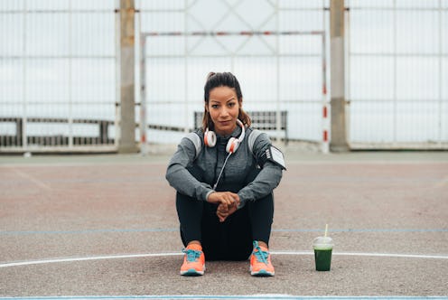 Relaxed fitness woman drinking detox green smoothie during outdoor city workout rest. Sport nutritio...