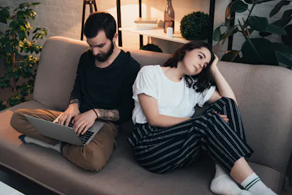 bored woman sitting on couch while man using laptop in living room