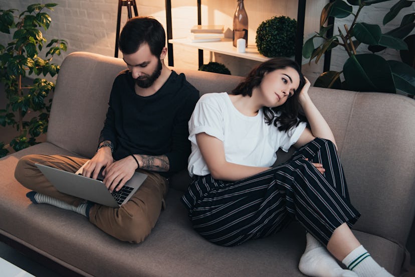 bored woman sitting on couch while man using laptop in living room