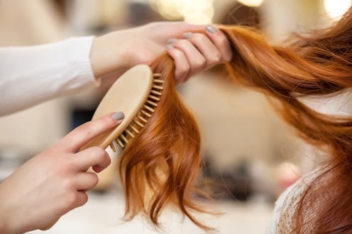 Hairdresser combing her long, red hair of his client in the beauty salon. Professional hair care and...