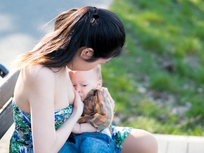 A young beautiful Asian mother is breastfeeding her newborn baby boy in nature outdoors in the park,...
