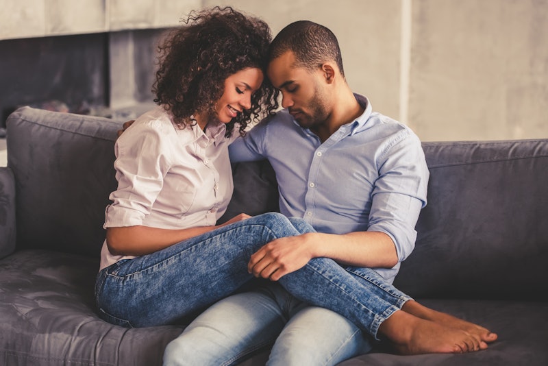 Beautiful young Afro American couple is hugging and smiling while sitting together on couch at home