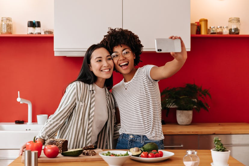 Girls smile and take selfie in kitchen. Woman in glasses and her friend are cooking dinner