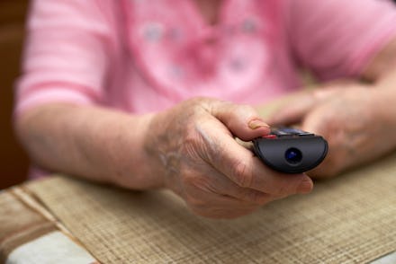 Elderly woman operating TV or DVD with remote control.