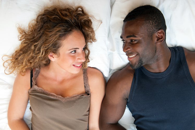Happy young couple lying in bed looking at each other, top view.