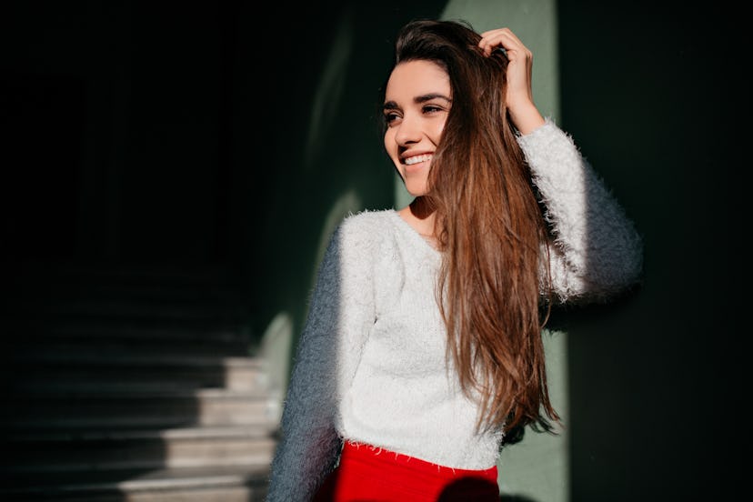 Fashionable girl with long brown hair looking away with cute smile. Indoor portrait of excited cauca...