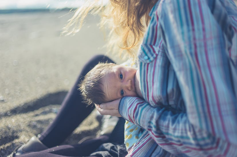 A young mother is breastfeeding her baby on the beach