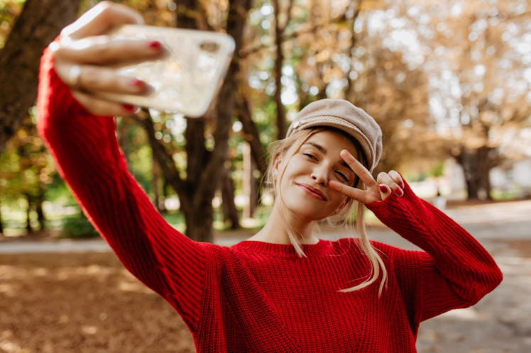 Young woman in nice red pullover make selfie on the park path.